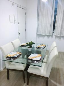 una mesa de cristal con dos sillas blancas y una mesa con comida. en Apartamento Copacabana, en Río de Janeiro