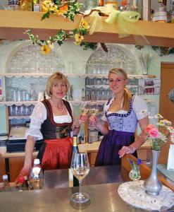 dos mujeres de pie detrás de un mostrador con copas de vino en Gasthof Weidmannshof, en Bresanona