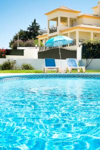 a swimming pool with two chairs and an umbrella and a house at Apartamentos Benvindo in Albufeira
