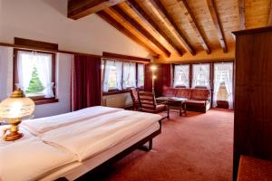 a bedroom with a bed and chairs and windows at Hotel Astoria in Zermatt