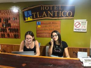 twee vrouwen die aan een bar zitten te praten op een mobiele telefoon bij Hotel Atlántico Residencial in Santa Teresita