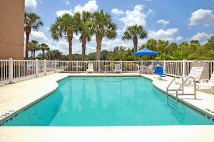a swimming pool with chairs and an umbrella and palm trees at Microtel Inn & Suites by Wyndham Bushnell in Bushnell