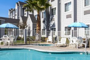 a swimming pool with chairs and umbrellas next to a building at Microtel Inn & Suites Modesto in Ceres