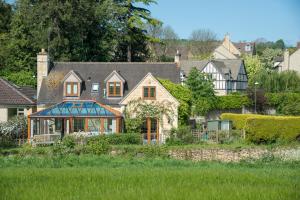 una grande casa in un cortile con un campo verde di Kingfisher Cottage a Winchcombe