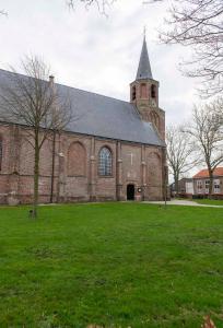 a large brick church with a steeple on a grass field at Studio Ana- Hata (vanuit het Hart ❤) in Gapinge