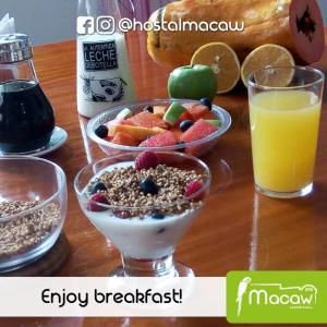 a table with bowls of cereal and fruit and a glass of orange juice at Hostal Macaw in Guayaquil