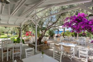eine Terrasse mit weißen Tischen und Stühlen und lila Blumen in der Unterkunft Limnonari double room in Skopelos