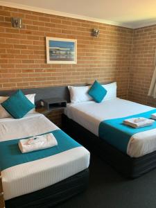 duas camas num quarto com uma parede de tijolos em The Oaks Hotel Motel em Albion Park