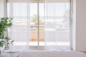 1 dormitorio con cortinas blancas y ventana grande en "PLAGE" Splendide Vue Mer depuis la chambre et le salon cuisine, 20m de la plage! en Canet-en-Roussillon
