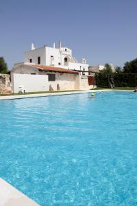 una grande piscina blu con una casa sullo sfondo di Masseria Madonna dell'Arco Agriturismo a Martina Franca