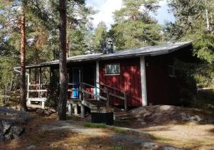 a red cabin in the woods with a porch at Björkholm mökit in Pargas