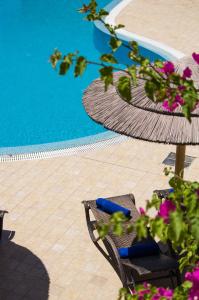 a pool with two chairs and an umbrella and flowers at Smaragdi in Perivolos