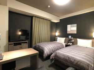 a hotel room with two beds and a flat screen tv at Hotel Route-Inn Koga Ekimae in Koga