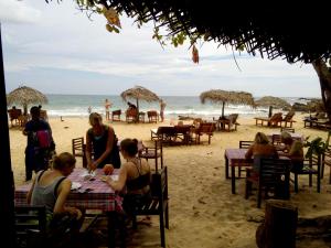 a group of people sitting at tables on the beach at Deshan Homestay & Restaurant in Tangalle
