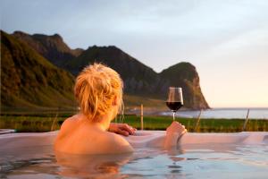 a woman is sitting in the water with a glass of wine at Unstad Arctic Surf in Unnstad