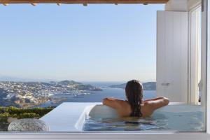 a woman sitting in a bath tub looking out a window at Amare Mykonos in Tourlos