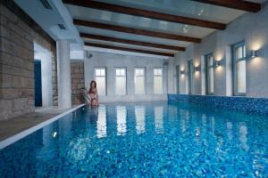 a woman is standing next to a swimming pool at Bukowy Park Hotel Medical SPA in Polanica-Zdrój