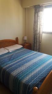1 dormitorio con 1 cama con manta azul y ventana en Edificio Riazor n° IX en San Clemente del Tuyú