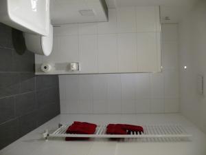 a white tiled bathroom with two red towels on a rack at Gästehaus Fraune in Salzkotten
