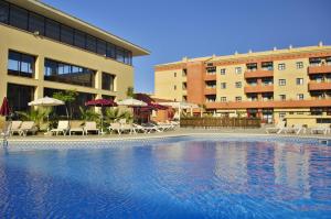 a swimming pool in front of a building with chairs and umbrellas at Leo Punta Umbría in Punta Umbría