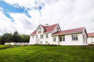 a white house with a red roof on a green field at Ósar Hostel in Vatnsnes