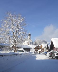 a snow covered village with a church and a tree at Landhotel zum Staffelwirt in Jachenau