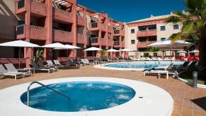 a swimming pool in front of a hotel with chairs and umbrellas at Leo Punta Umbría - Adults Only in Punta Umbría