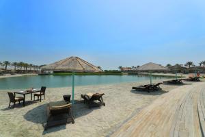 Al Bander Hotel & Resort في سترة: شاطئ فيه كراسي وطاولة وبعض الماء
