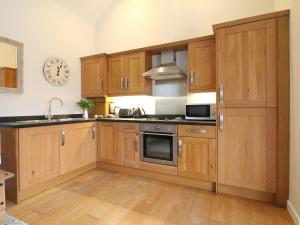 una cocina con armarios de madera y un reloj en la pared en Hazel Barn, en Falmouth 14 fotos más