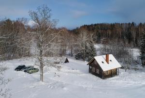 Cabaña de madera pequeña en la nieve con coche en Jaunlidumnieki, en Mālpils