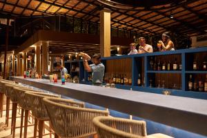 a bartender at a bar with chairs and people at Bandara Spa Resort & Pool Villas, Samui in Bophut