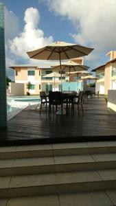 una terraza de madera con mesa, sillas y sombrilla en Casa Recanto de Guarajuba, en Guarajuba
