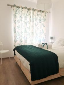 a bedroom with a bed with a green blanket and a window at Simply@Home in Setúbal