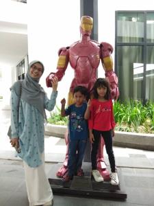Une femme et deux enfants debout à côté d'une statue de super-héros dans l'établissement Tini Icity Guesthouse, à Shah Alam