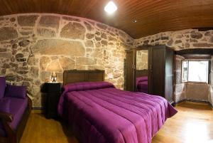 1 dormitorio con cama morada y pared de piedra en Casa Dos Fuelles en Ourense