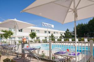 un patio con mesas y sombrillas junto a una piscina en Novotel Amiens Pôle Jules Verne, en Boves