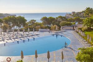 una piscina con sillas y sombrillas y el océano en Blau PortoPetro Beach Resort & Spa, en Portopetro