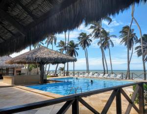 a swimming pool with palm trees and the ocean at Studio 230 Eco Paradise Cumbuco in Cumbuco