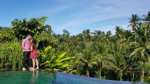 a man and woman standing on the edge of a swimming pool at Puri Sebali Resort in Ubud