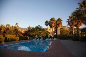 a swimming pool with palm trees and a house in the background at Nebrodi Park Private Villa in SantʼAgata di Militello