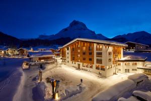 ein Gebäude im Schnee mit einem Berg im Hintergrund in der Unterkunft Hotel Auriga in Lech am Arlberg