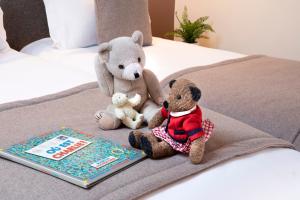Dois ursos de peluche sentados numa cama ao lado de um livro. em Hotel Brady - Gare de l'Est em Paris