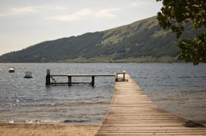 a wooden pier on a lake with mountains in the background at Caol Gleann Lodge in Rowardennan