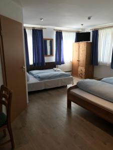 a bedroom with two beds and a chair and blue curtains at Hotel Guntia Boardinghouse in Günzburg