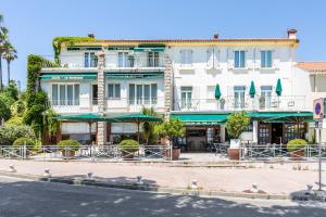 un grand bâtiment blanc avec des parasols verts dans une rue dans l'établissement Hôtel Le Richiardi, à Carqueiranne