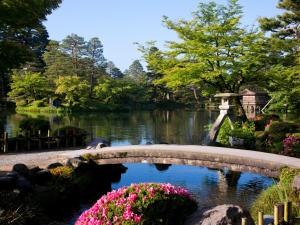 APA Hotel Kanazawa Chuo في كانازاوا: جسر فوق بركة في حديقة بها زهور