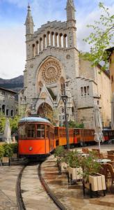 an orange train on tracks in front of a church at Sa caseta Farinera in Sóller