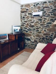 Habitación con pared de piedra, sofá y TV. en Casa Nazare en Vilar Torpim