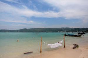 a hammock on a beach with a boat in the water at Phi Phi CoCo Beach Resort in Phi Phi Islands