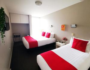 two beds in a hotel room with red and white sheets at Belmont Motor Inn in Christchurch